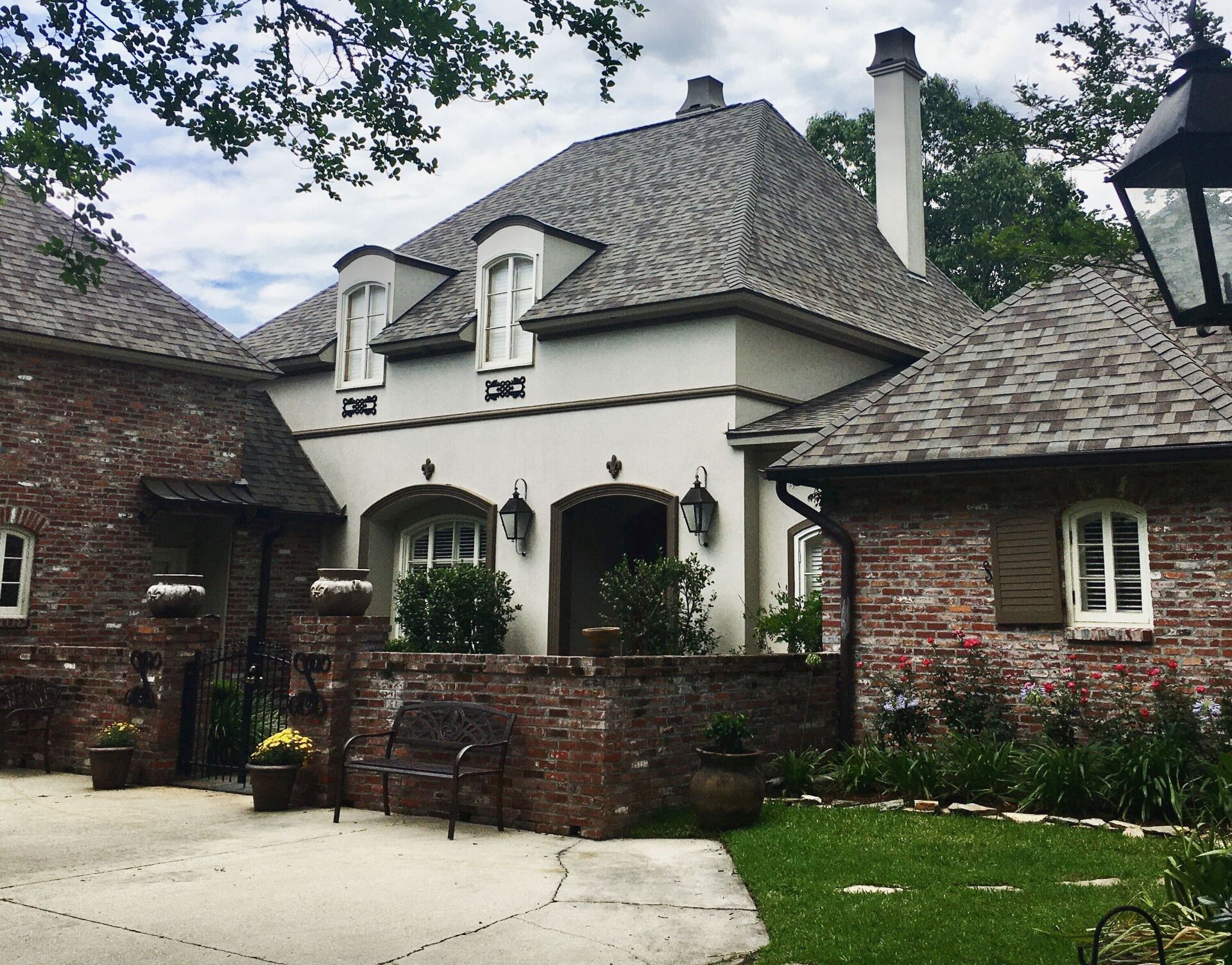 Brick and stucco house with a tiled roof, arched doorway, and a brick wall in front.
