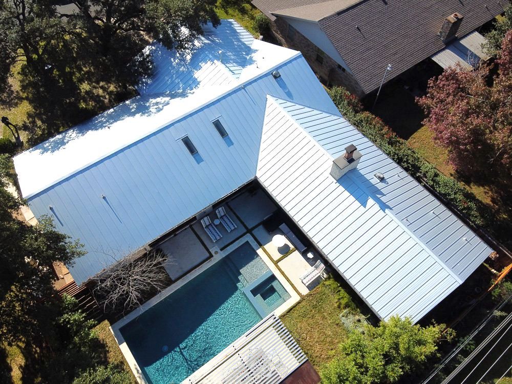 Aerial view of a modern white house with a central courtyard and blue swimming pool
