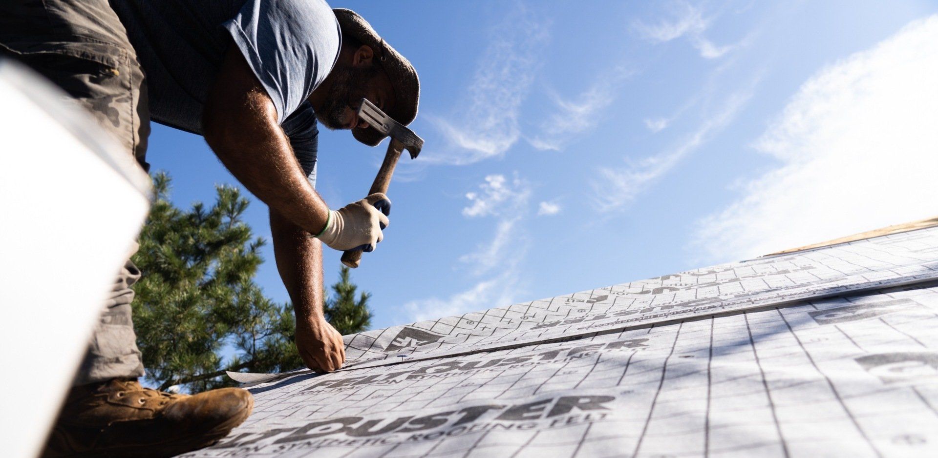 Sunny photo of a roofer applying underlayment to a new roof