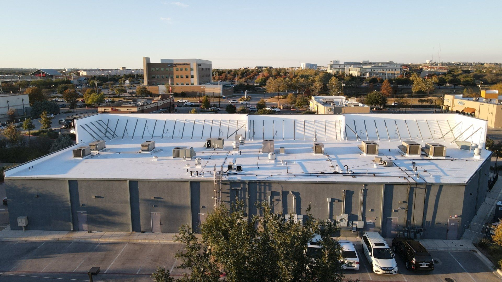 White flat-roofed commercial building with parked cars in front, seen from above at sunset