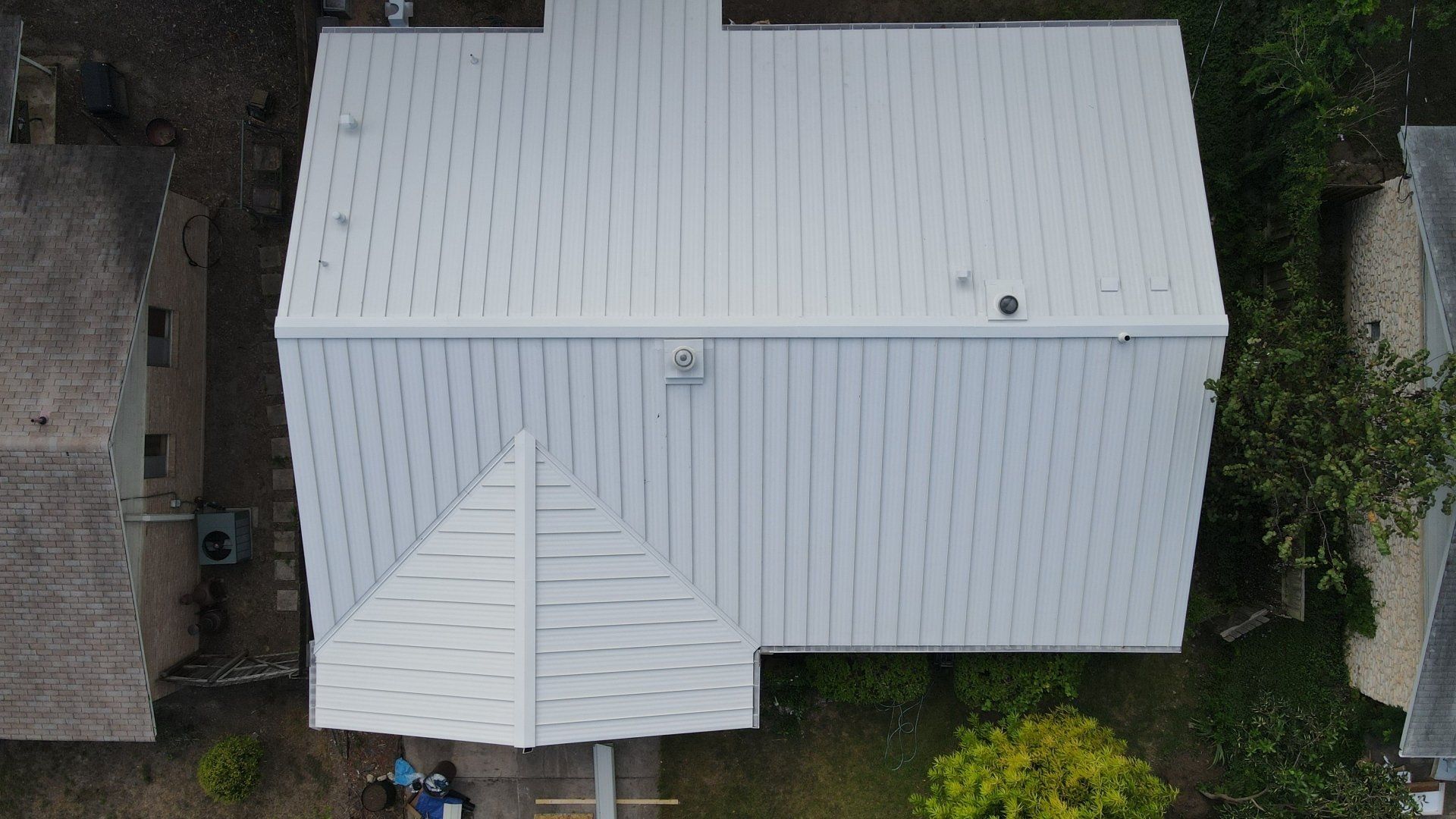 Aerial view of a white metal roof on a house surrounded by trees and neighboring buildings