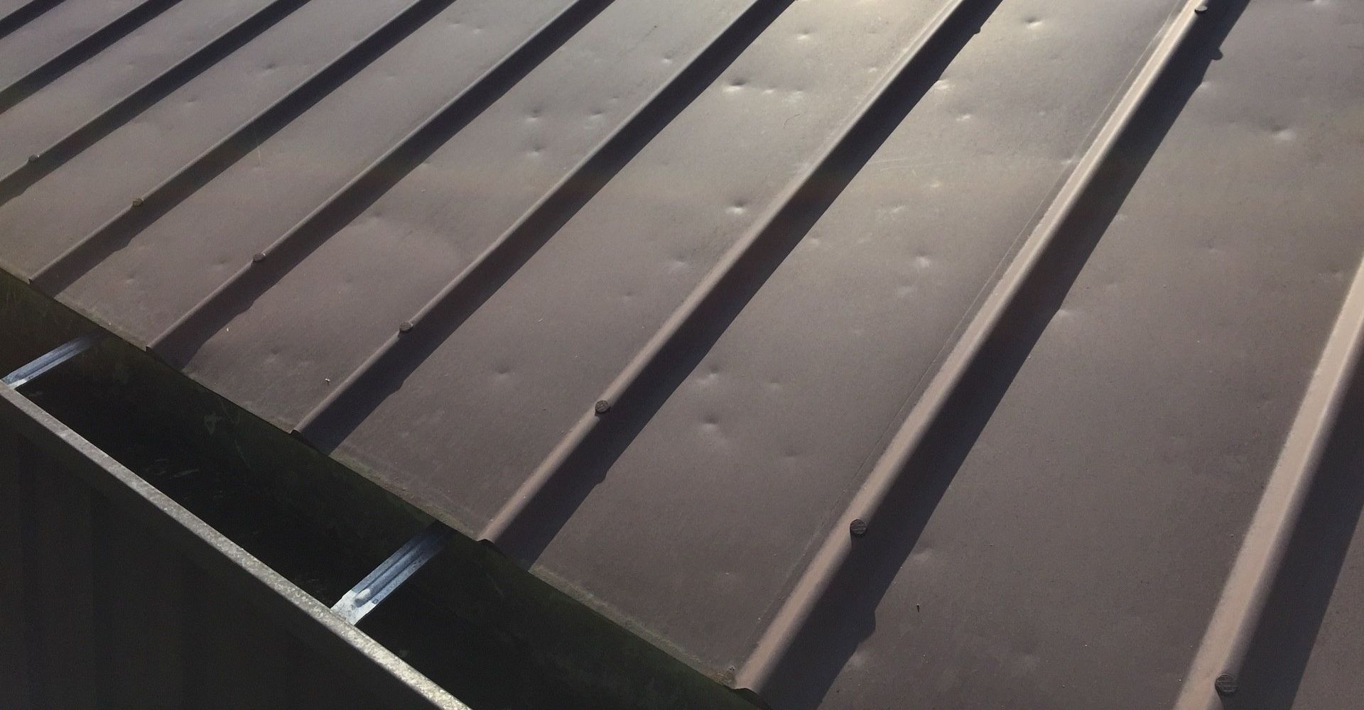 Close-up of a dark metal roof with parallel ridges and hail damage.