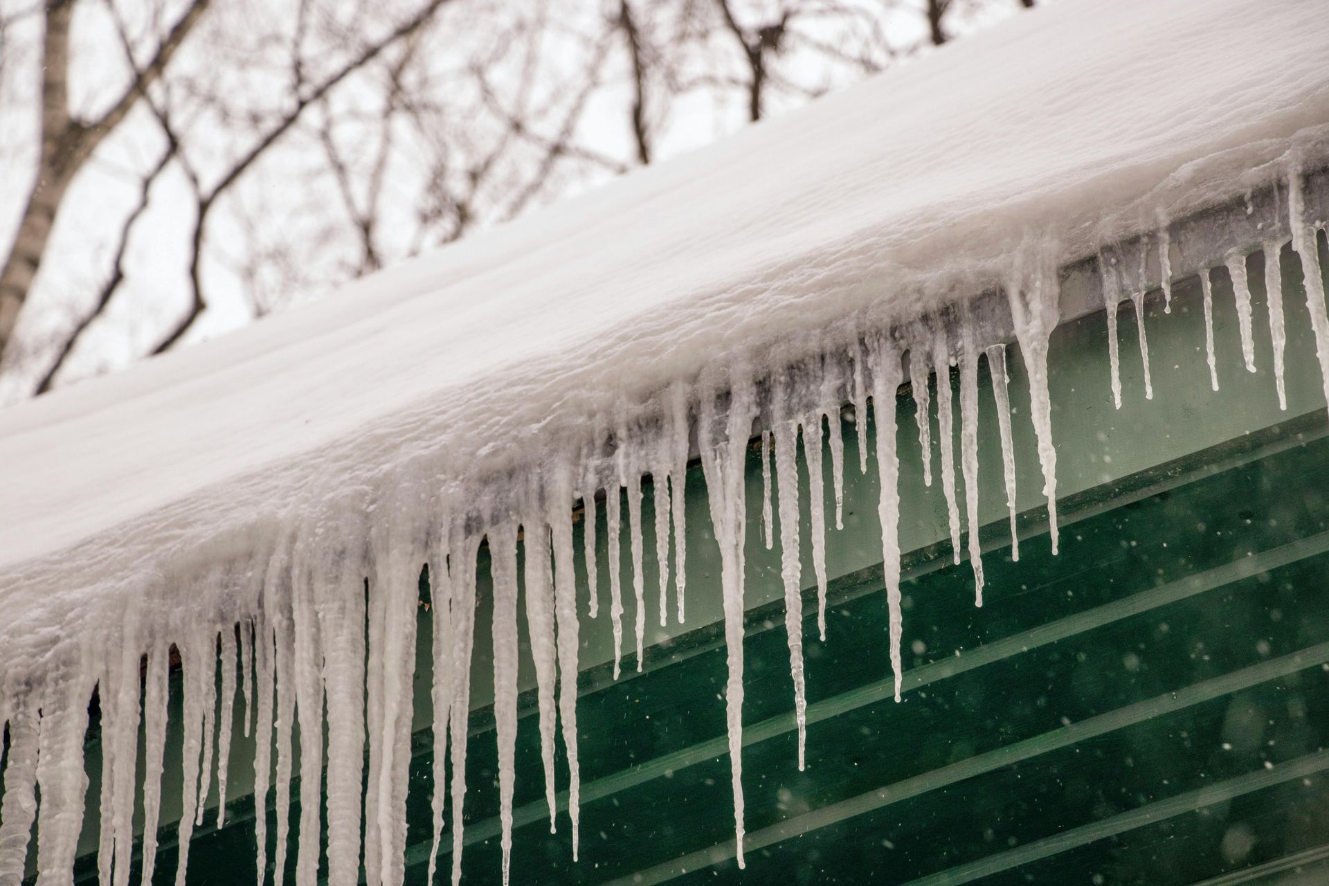 Icicles hanging from a green roof with snow; winter scene.