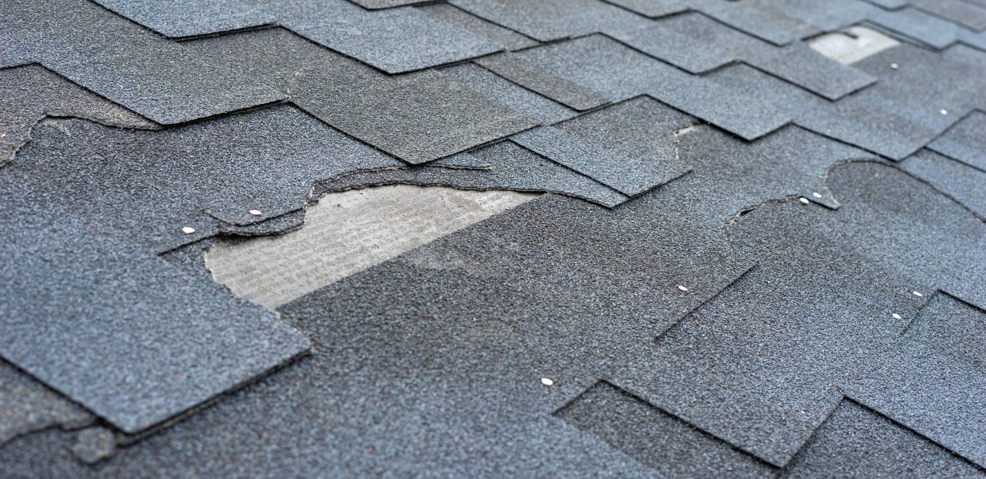 Damaged asphalt roof shingles with missing and torn sections.