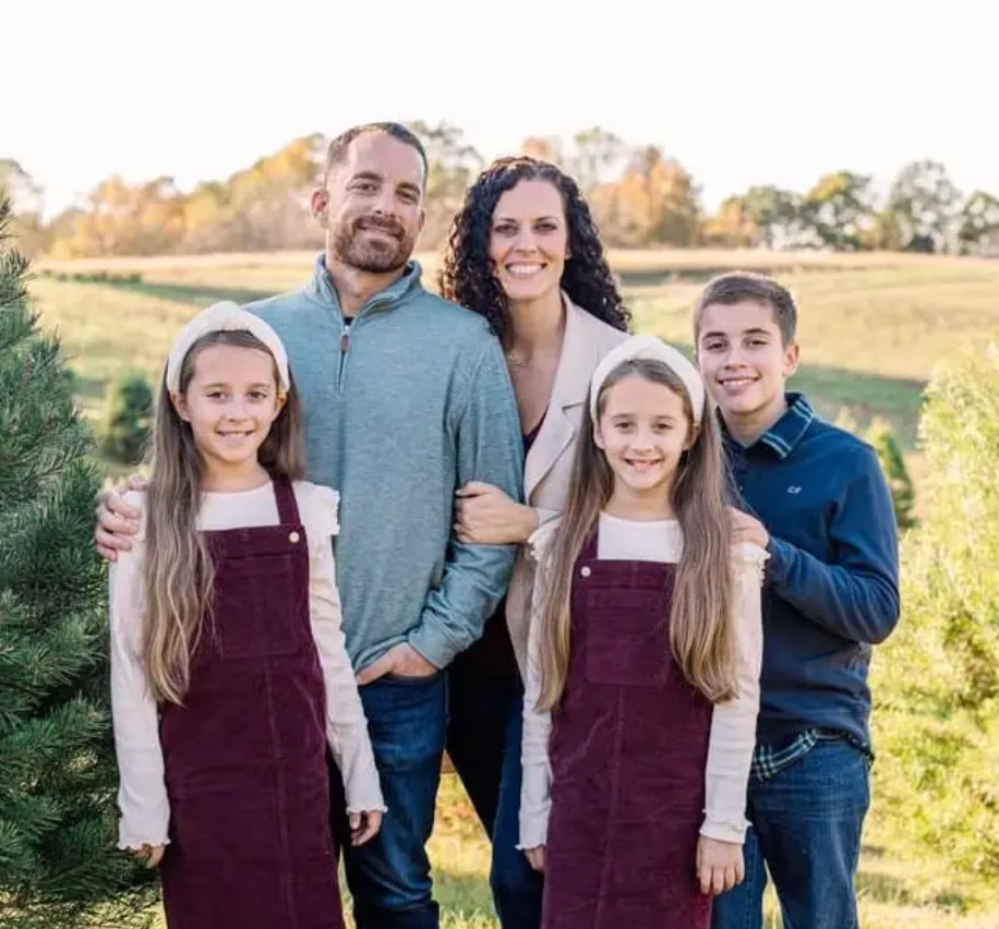 Family of five standing together in a sunny field, smiling at the camera.