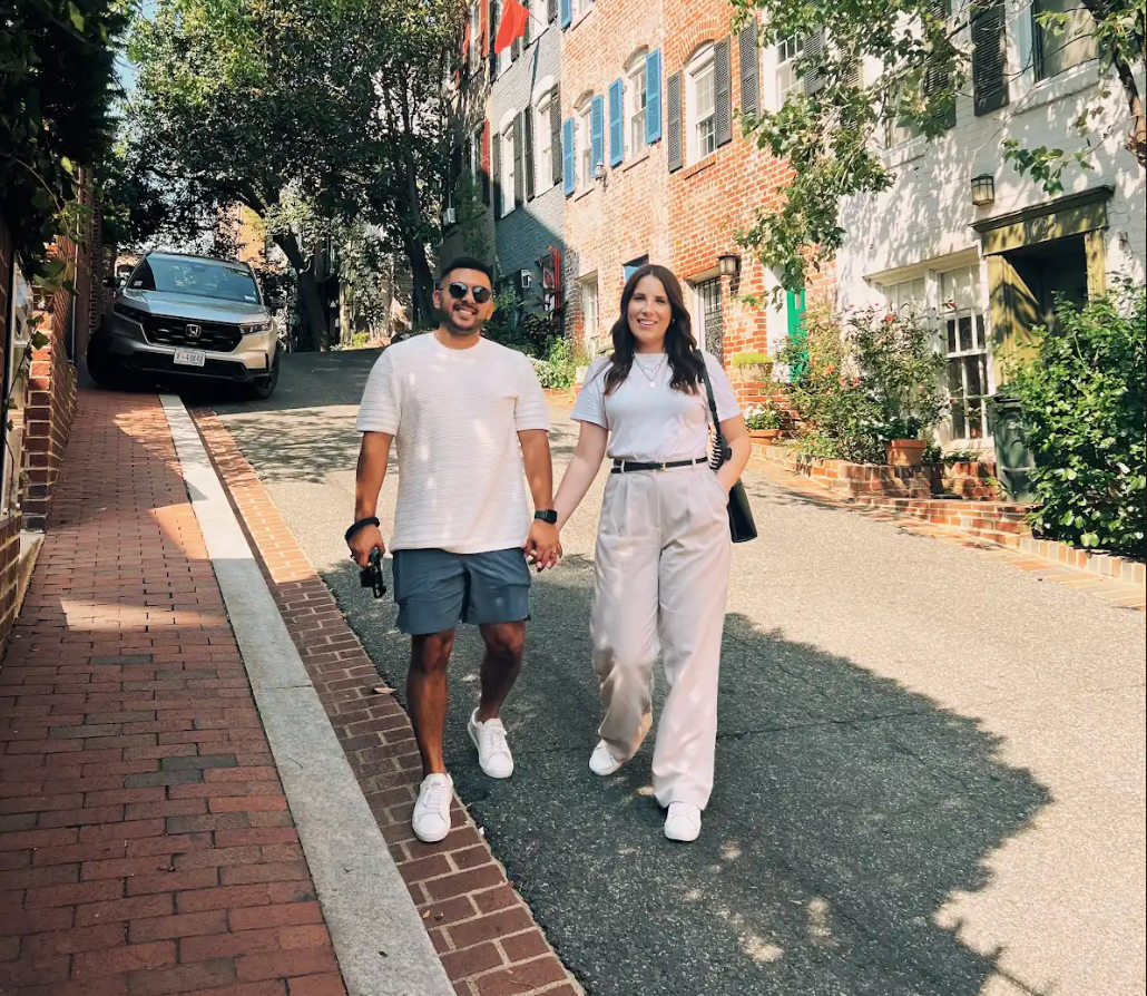Two people walking hand in hand down a sunny brick-lined street, smiling.