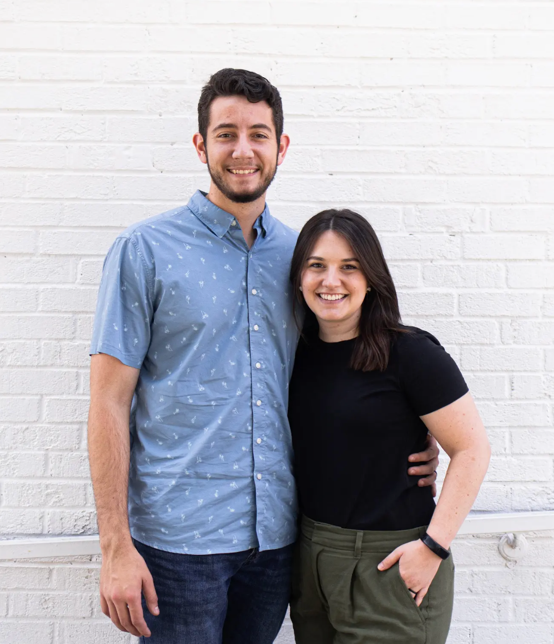 Smiling family of four standing against a textured wall, two adults behind two children.