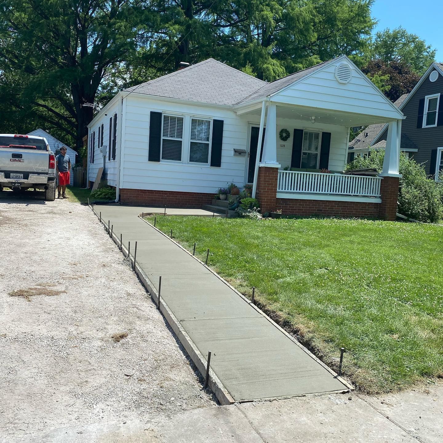 Freshly poured concrete walkway leading to a white house with a porch, green lawn on the right.