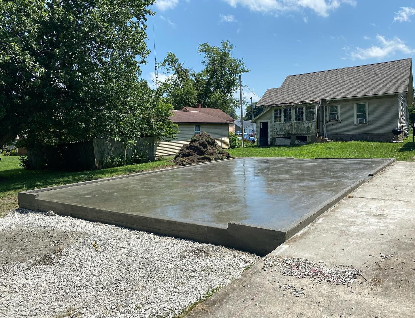 Newly poured concrete slab; gray blocks form the border, house and trees in background.