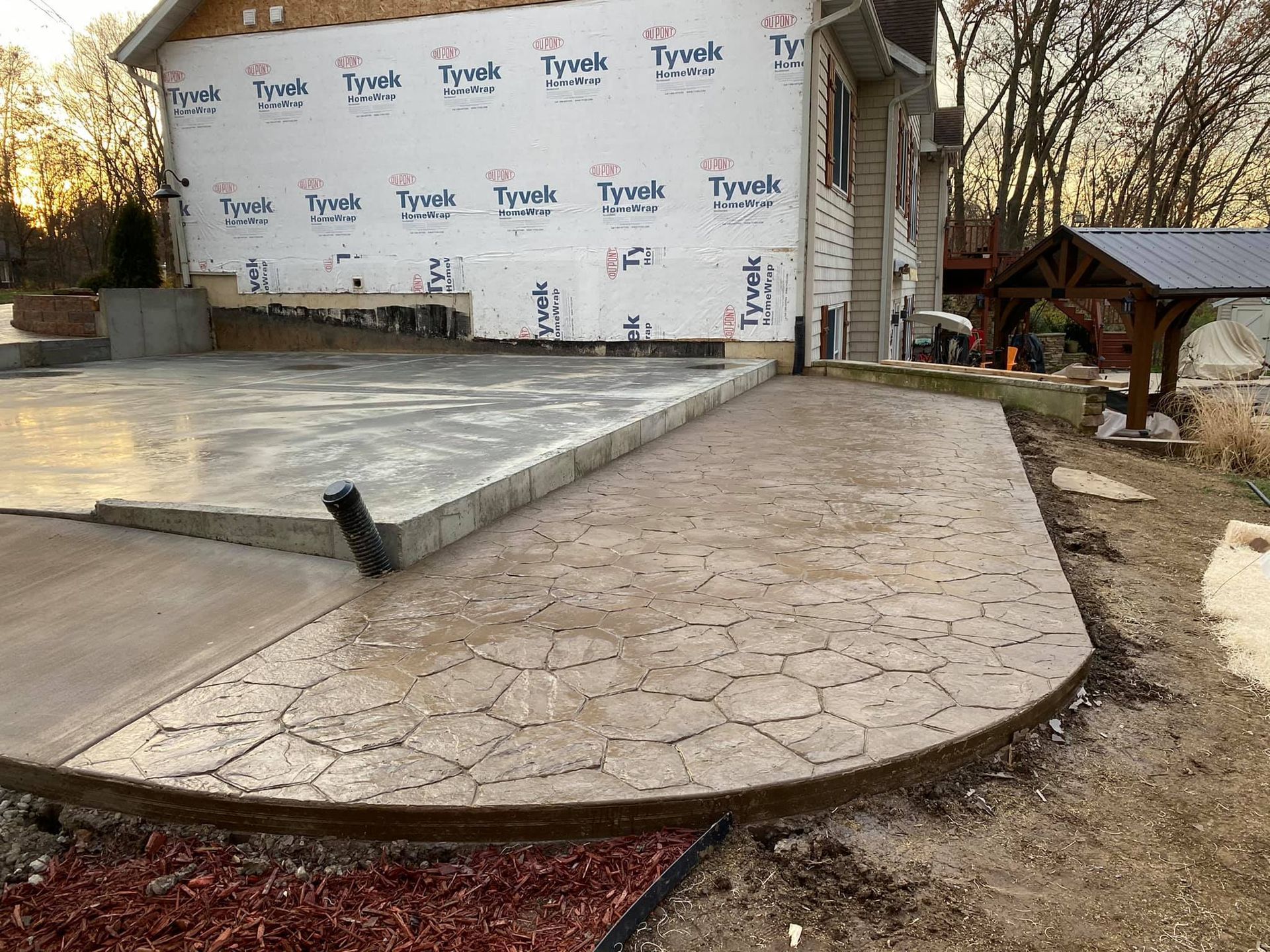 Concrete patio with stamped stone pattern, beside house with Tyvek.