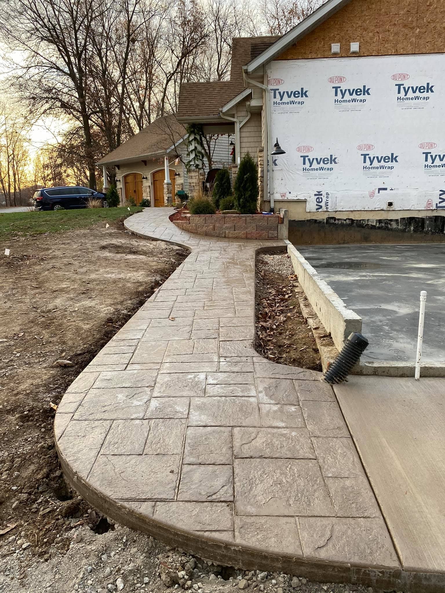 Stamped concrete pathway curves towards a house with garage. The house has a Tyvek-wrapped addition.