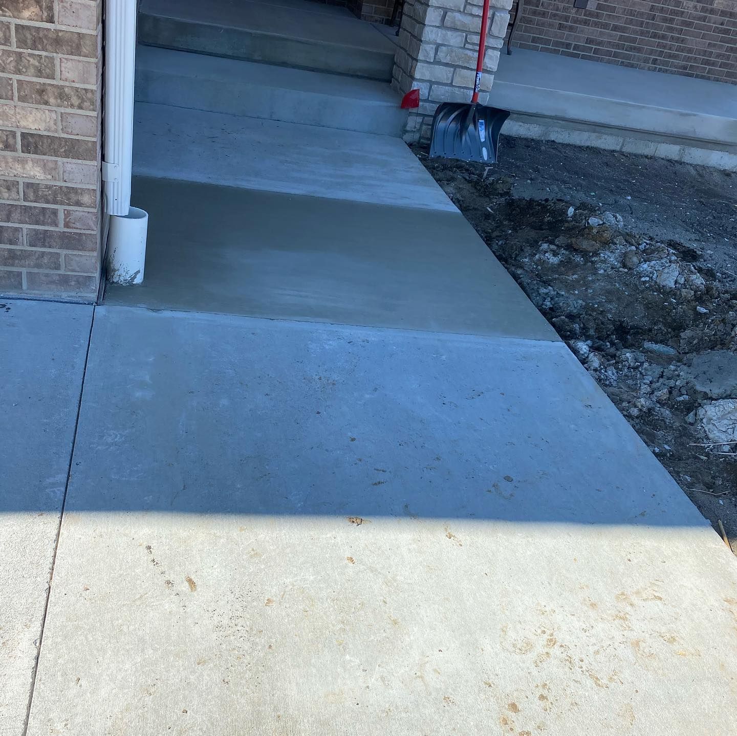 A freshly poured concrete walkway leading to a doorway, alongside a brick wall.