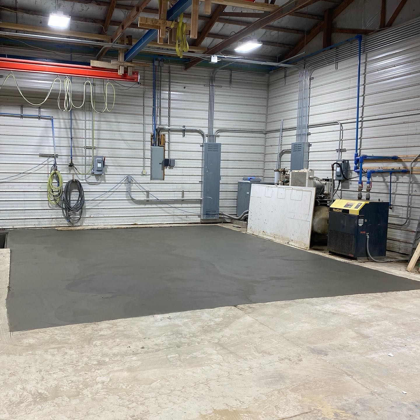 Freshly poured concrete section in a workshop. Metal walls, exposed pipes, and equipment surround it.