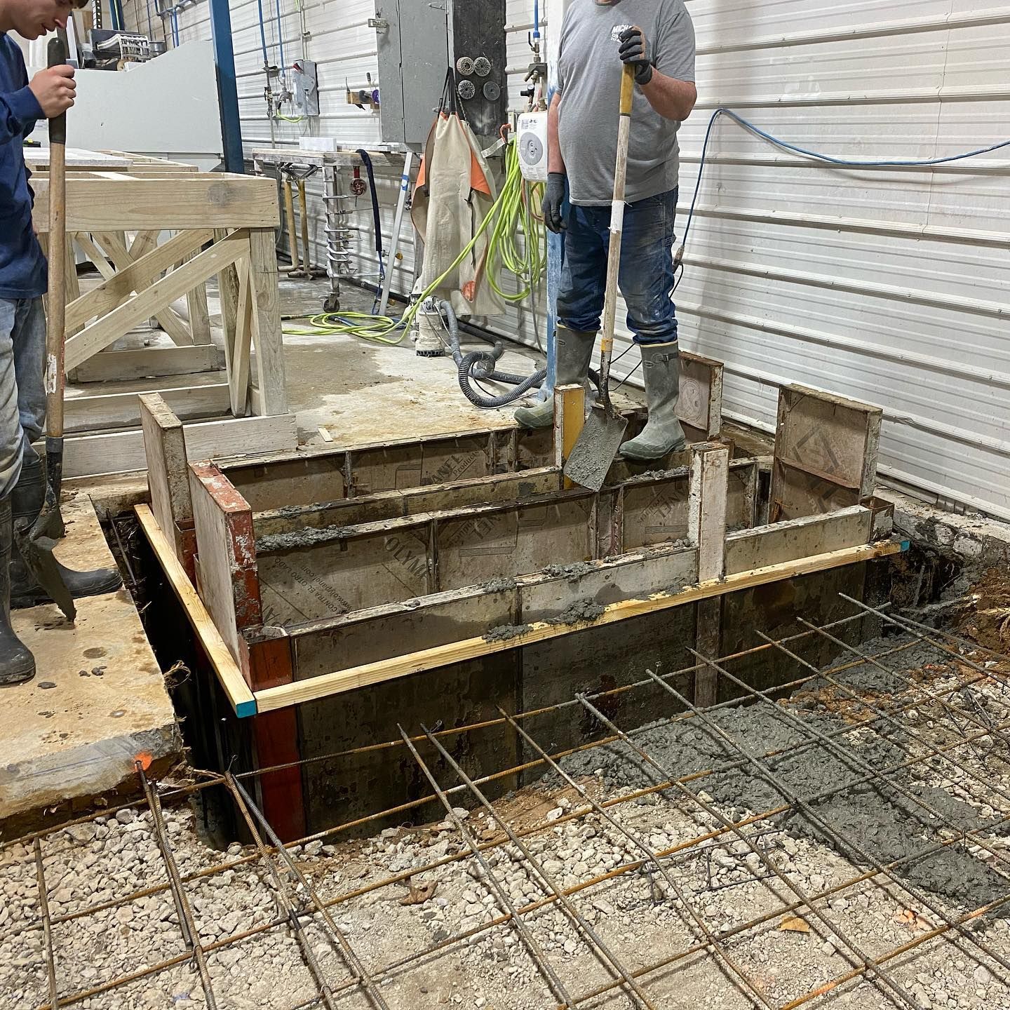Workers pouring concrete into a form. Steel rebar grid on floor, with wood forms for a raised section.