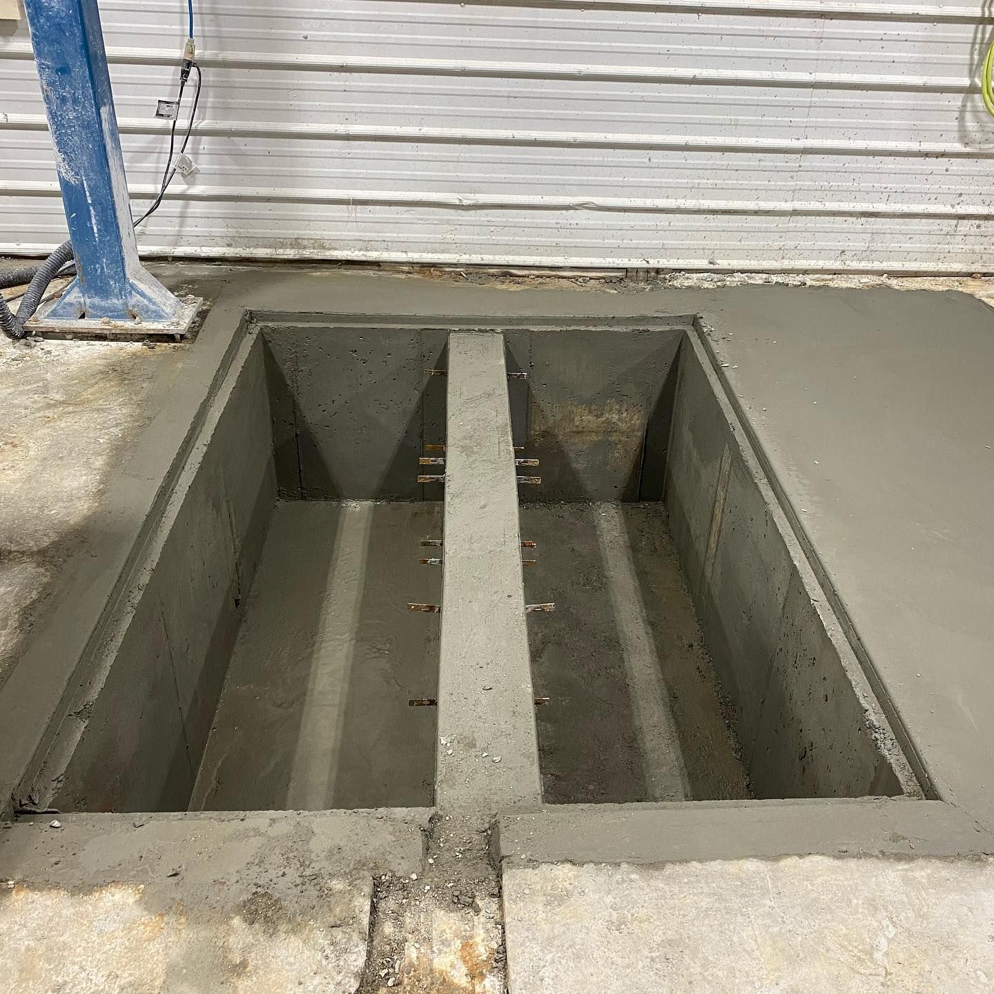Concrete car lift pit in a garage setting, freshly poured concrete, blue lift support visible.