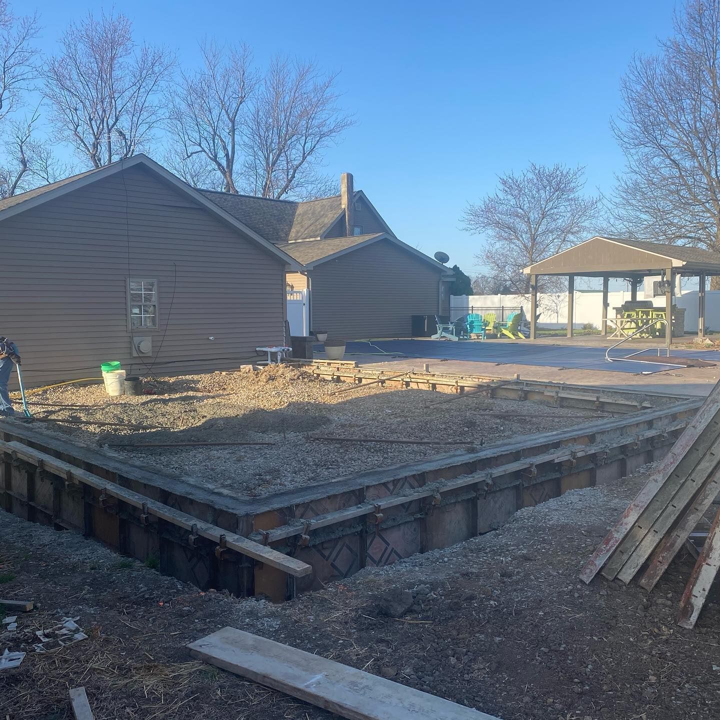 Construction site with wooden forms for foundation, gravel, house in background.