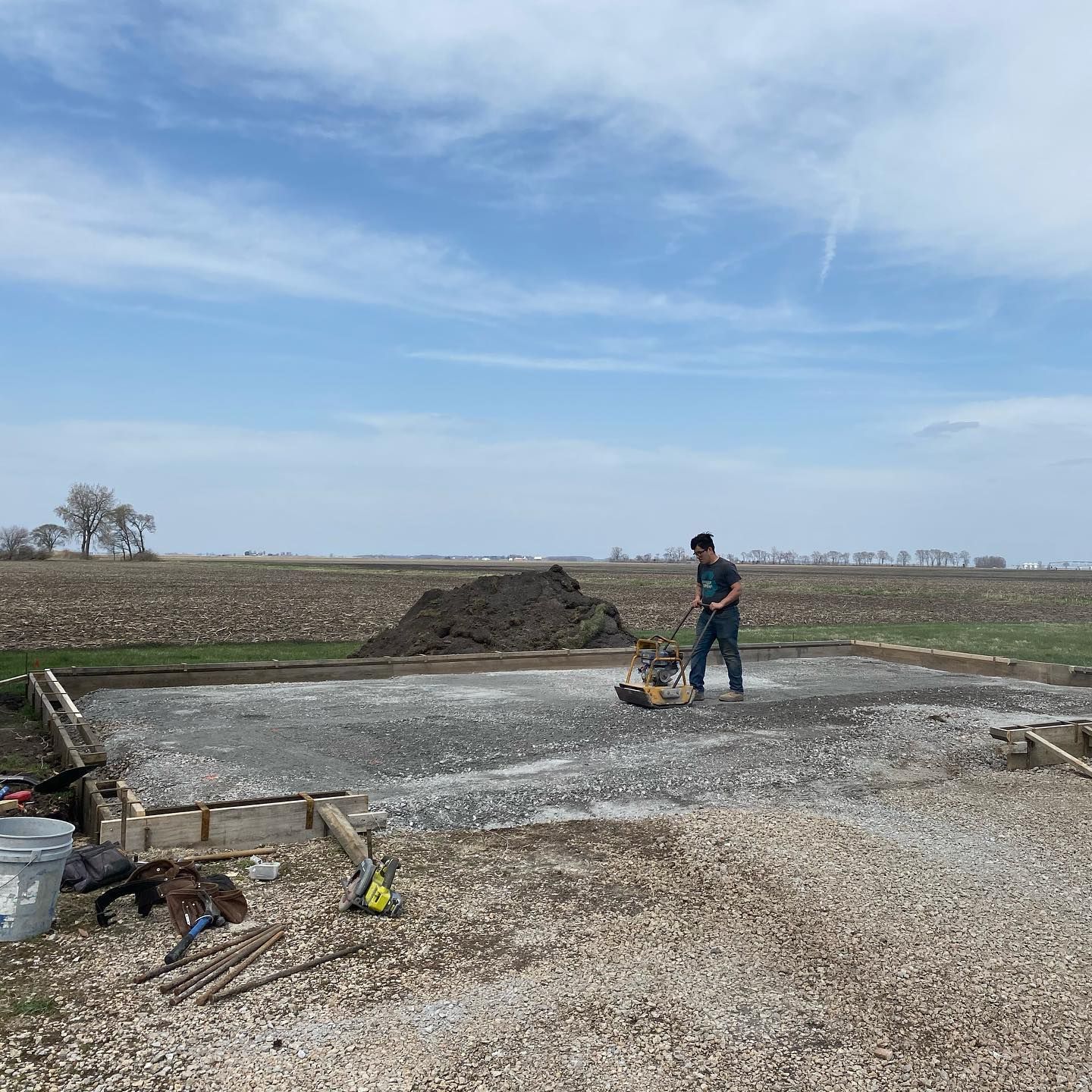 A person compacting gravel with a machine for a construction project on a rural property.