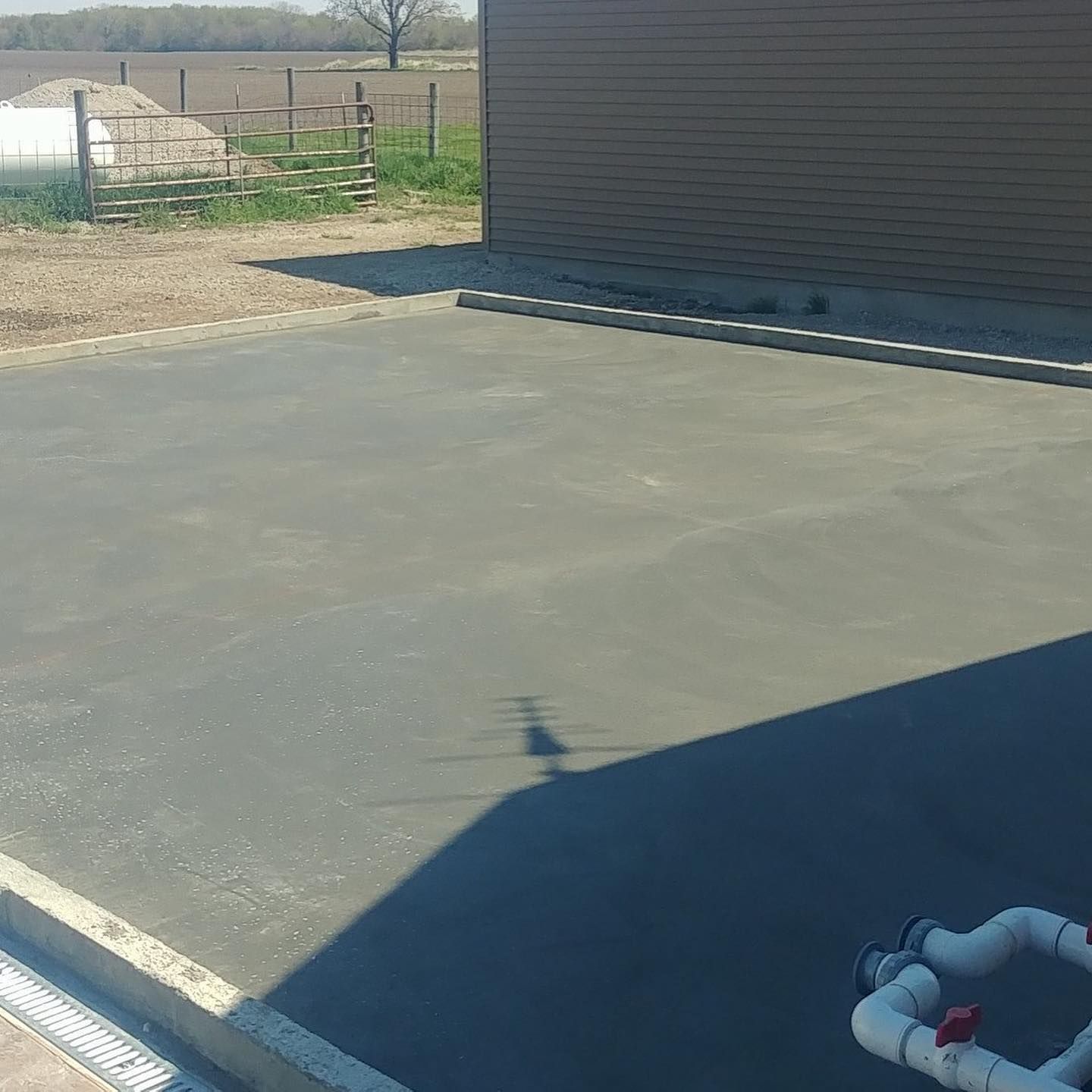 A smooth, gray concrete patio next to a brown building with agricultural landscape in the background.