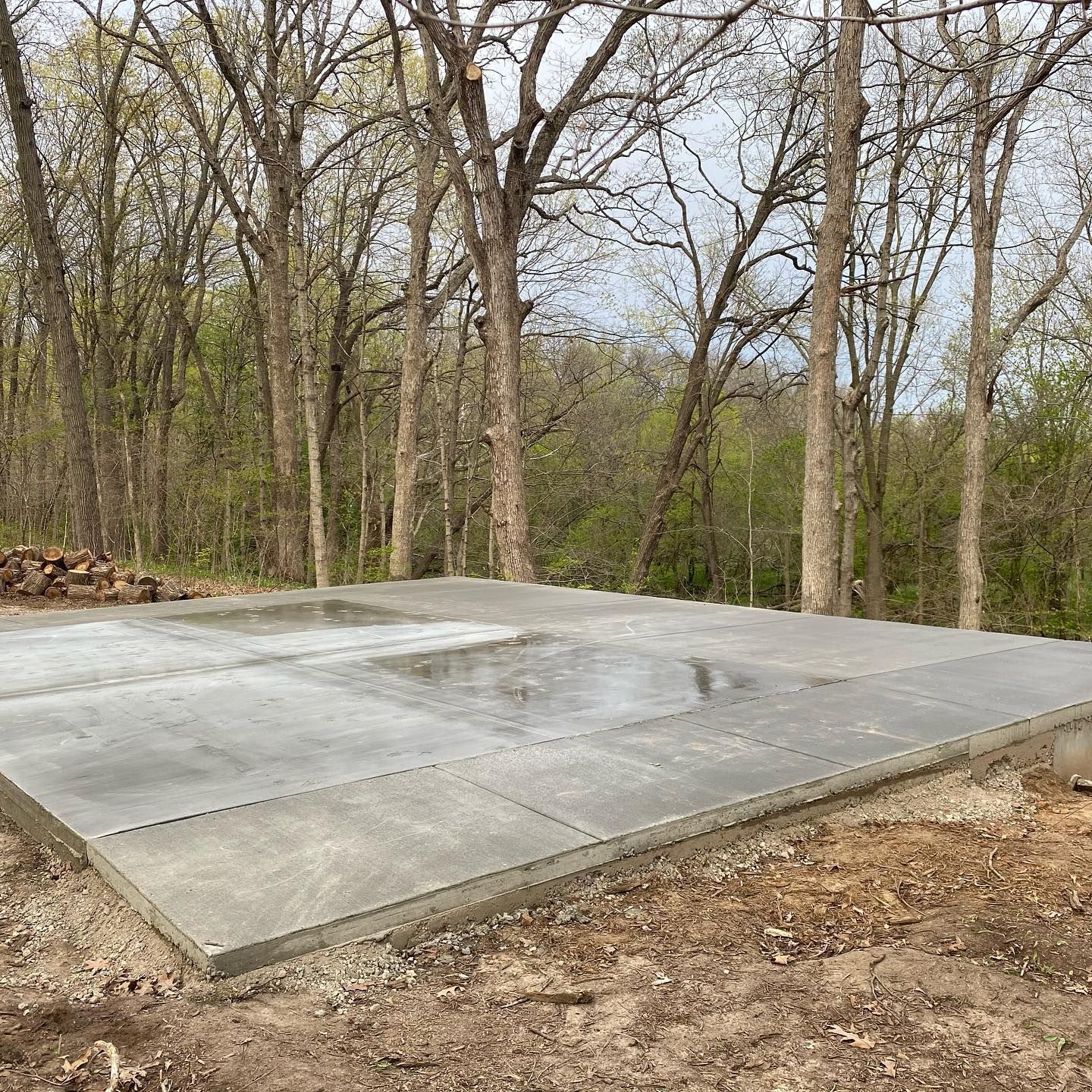 A concrete foundation for a building in a wooded area, with trees in the background.