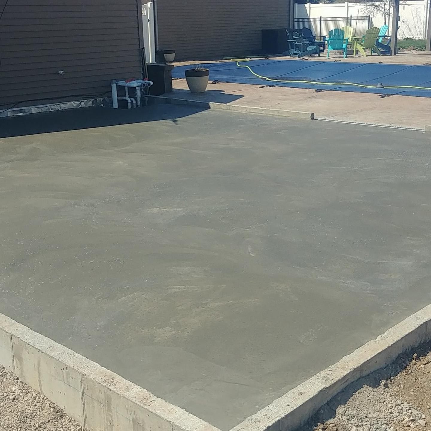 Newly poured concrete patio next to a brown house with a retaining wall and gravel border.