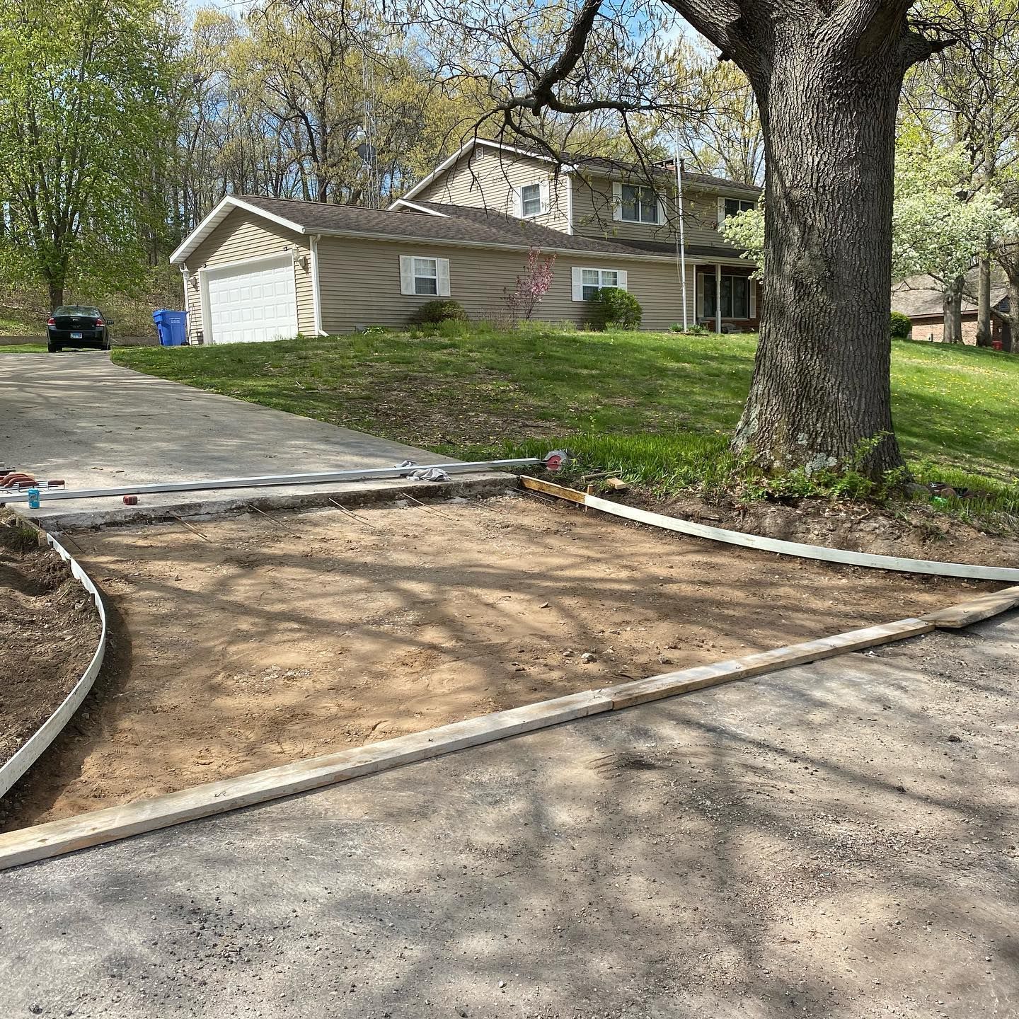 Driveway with a concrete border, excavated area for new paving, house in the background.