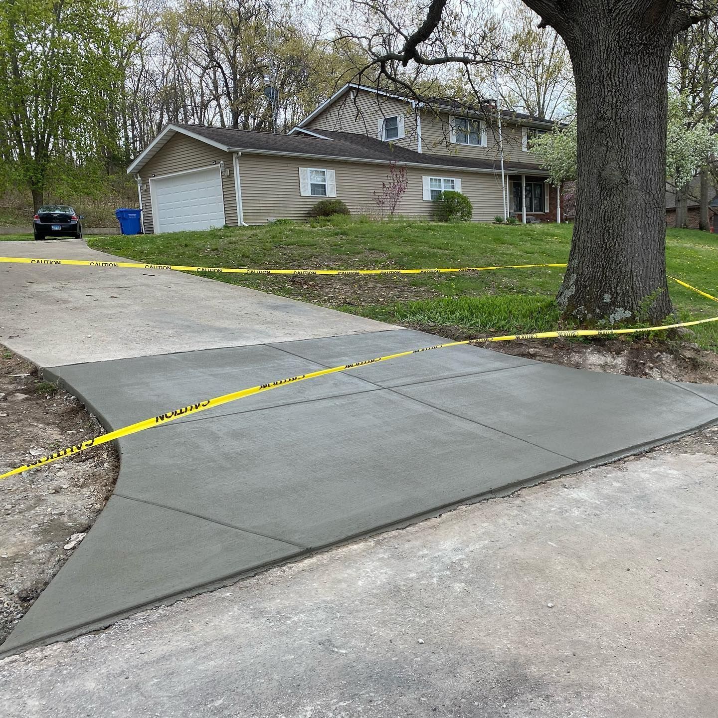 Newly poured concrete driveway with yellow caution tape, leading to a two-story house.