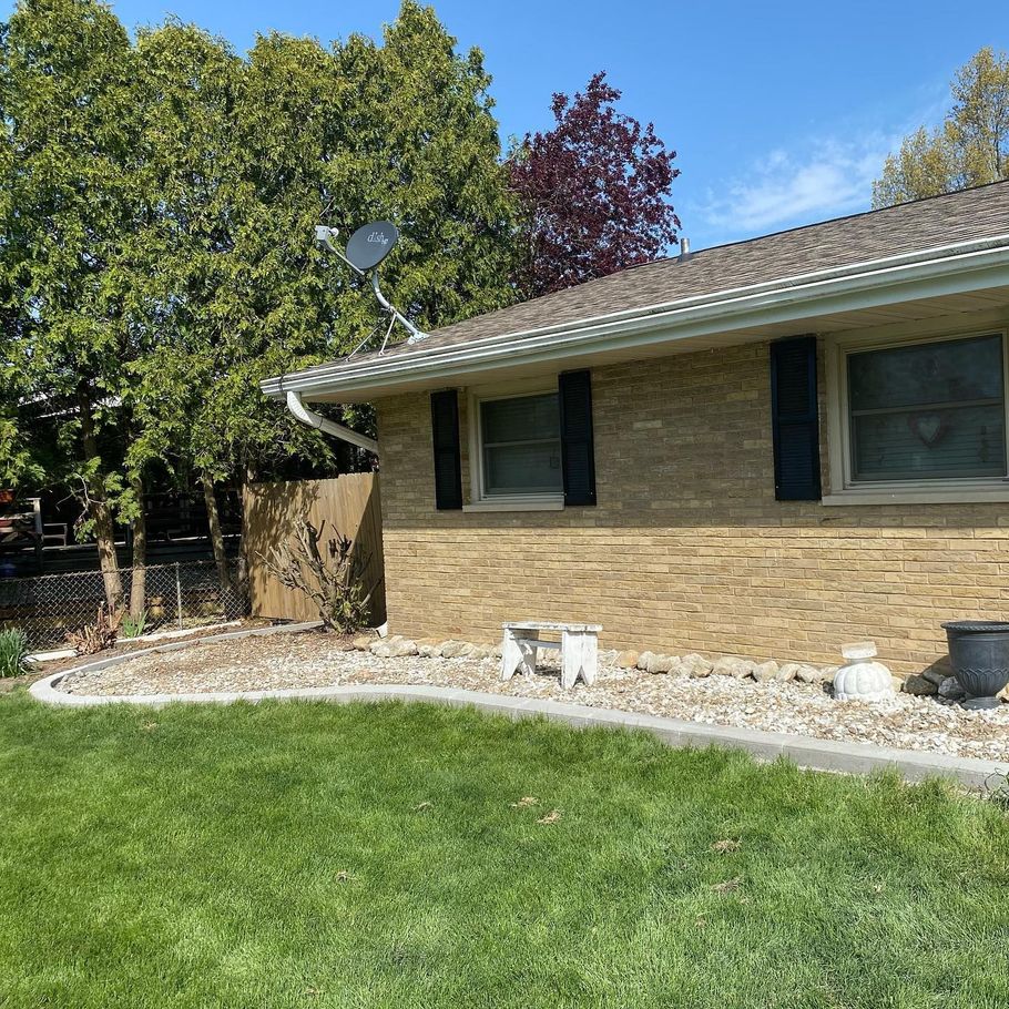 Tan brick house with black shutters, satellite dish, and green grass.