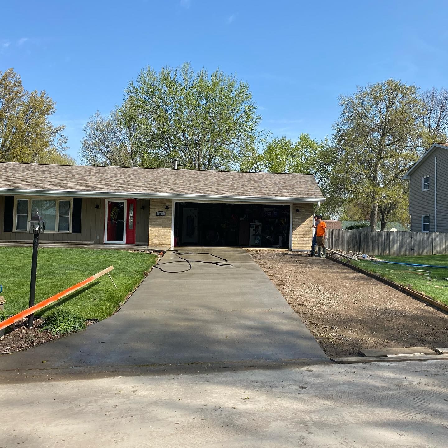 New concrete driveway with a man working; house with red door in background.