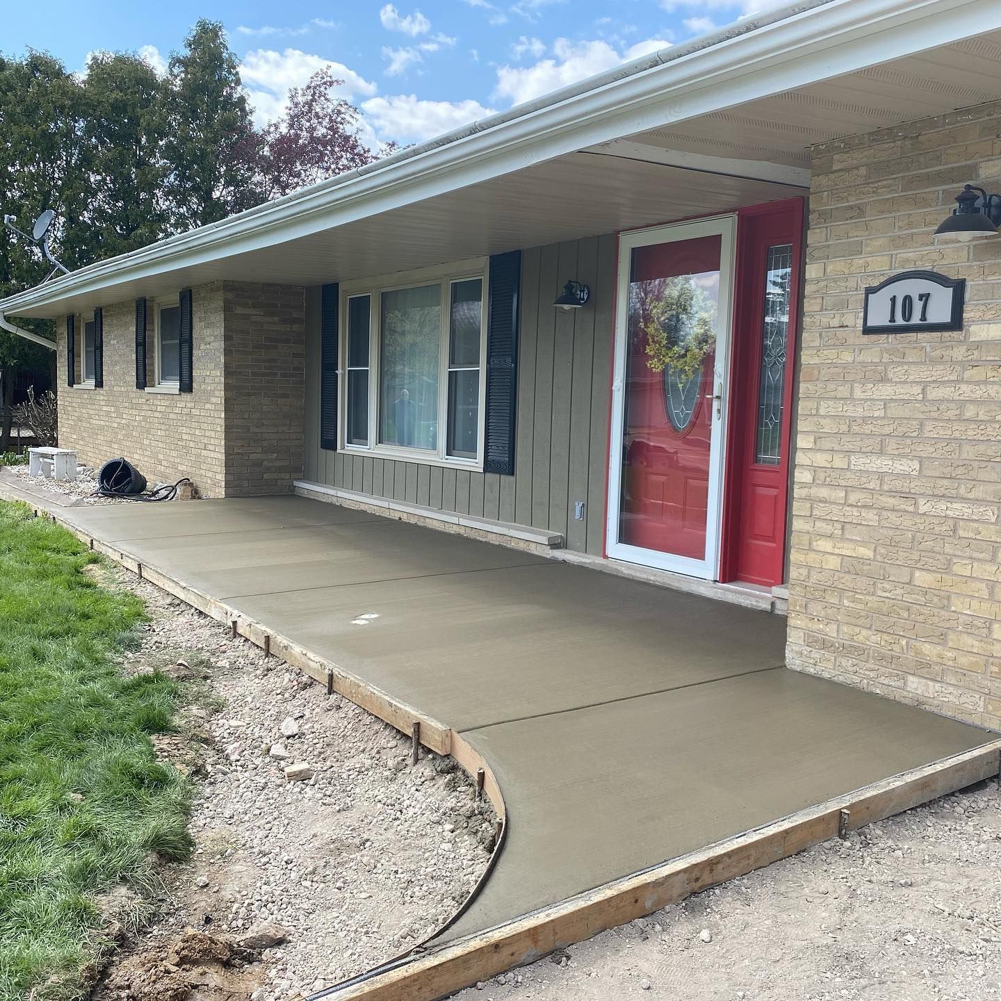 New concrete porch with wooden borders next to a house with a red door and brick exterior.