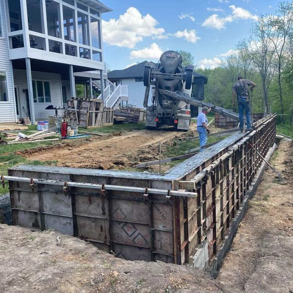 Construction site with concrete forms being filled by a cement truck, near a house.
