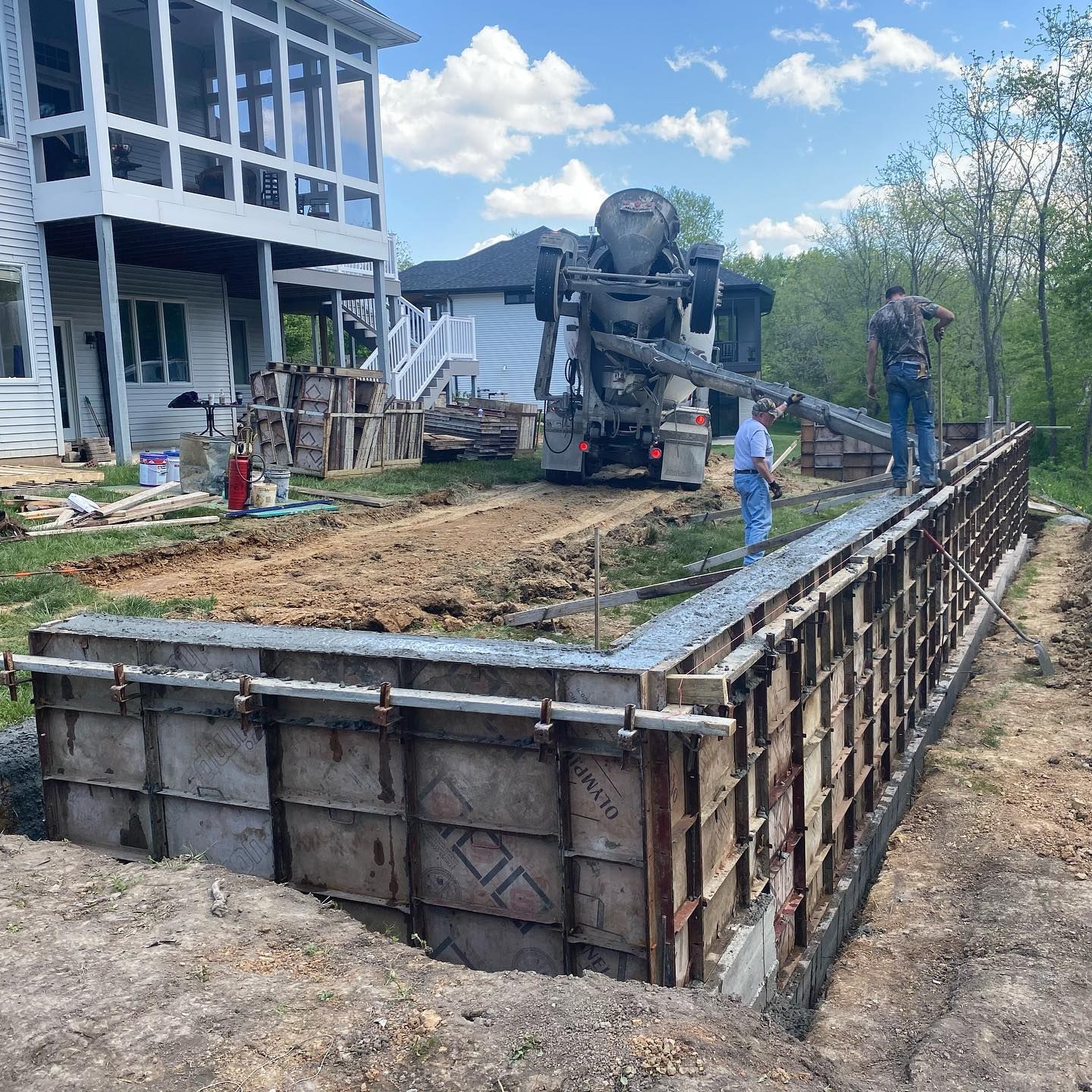 Concrete truck pouring cement into forms for a wall at a construction site near a house.