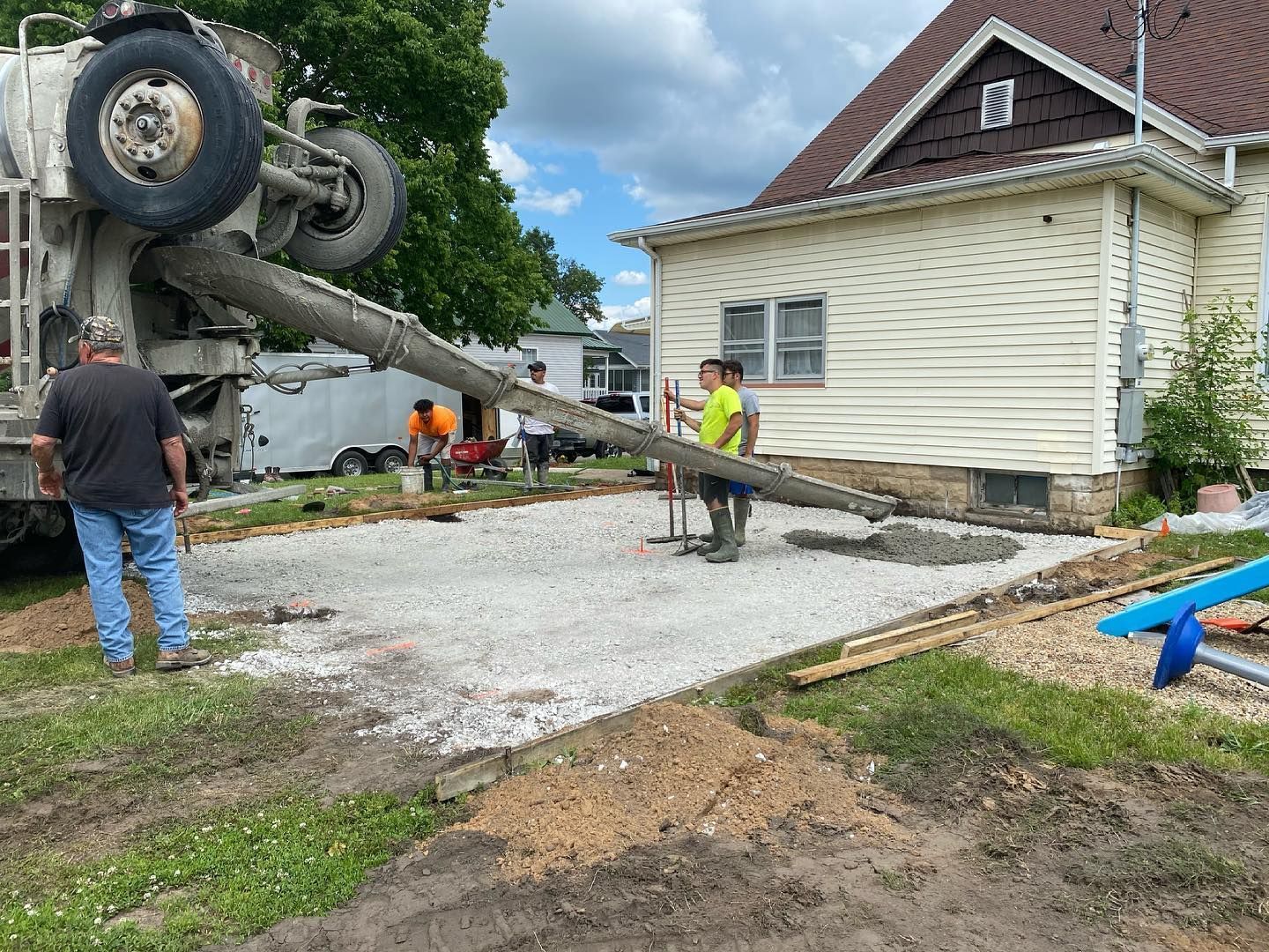 Cement truck pouring concrete for a driveway next to a house; workers are present.
