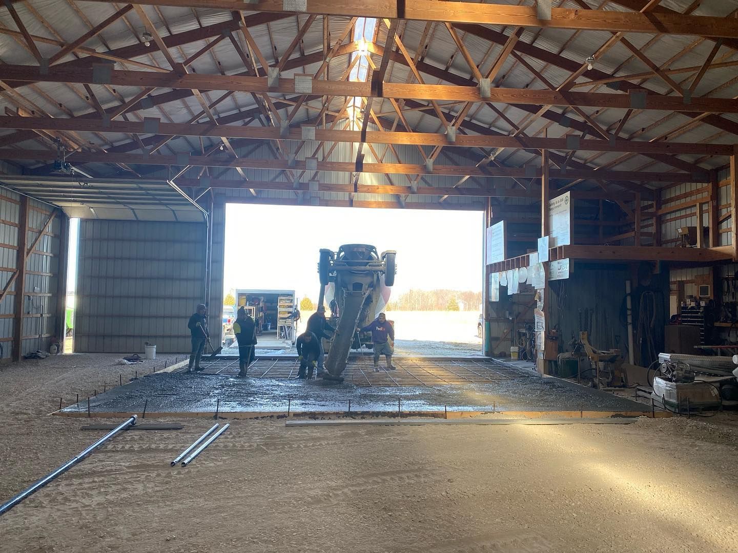 Cement truck pouring concrete into barn, with workers nearby.