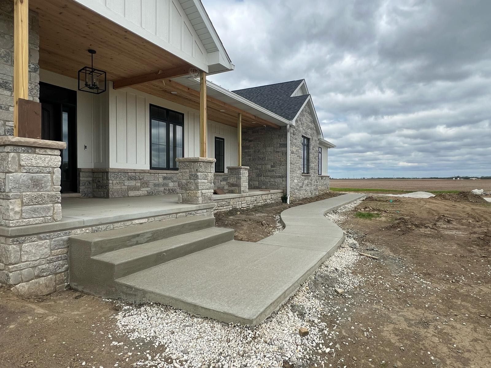 New home with gray stone and white siding, concrete porch, and overcast sky.