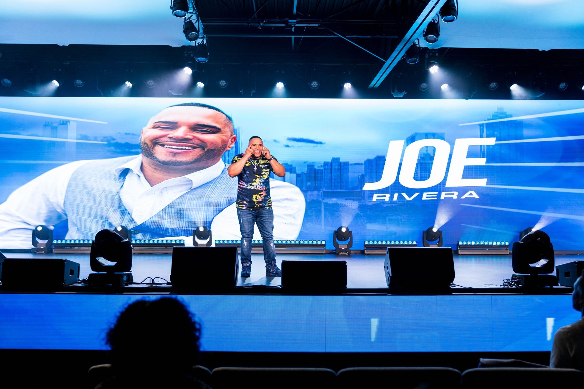 Joe Rivera on stage, giving a presentation in front of a large screen displaying his name and photo.