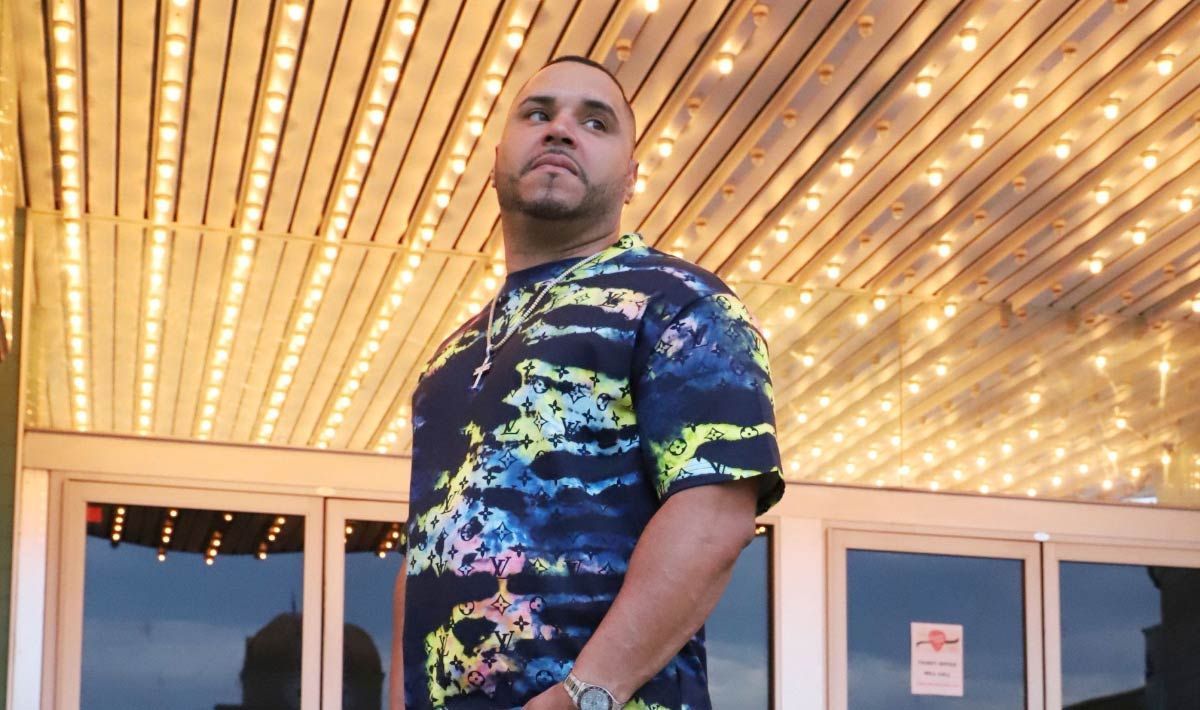 Man in tie-dye shirt standing under marquee lights.
