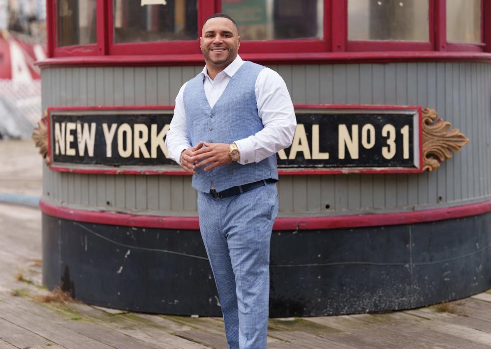 Man in blue suit stands in front of a sign that reads