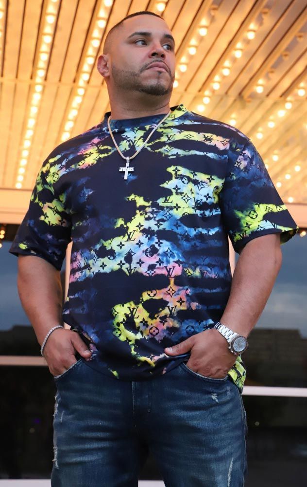 Man in colorful shirt, hands in pockets, stands outside illuminated building.