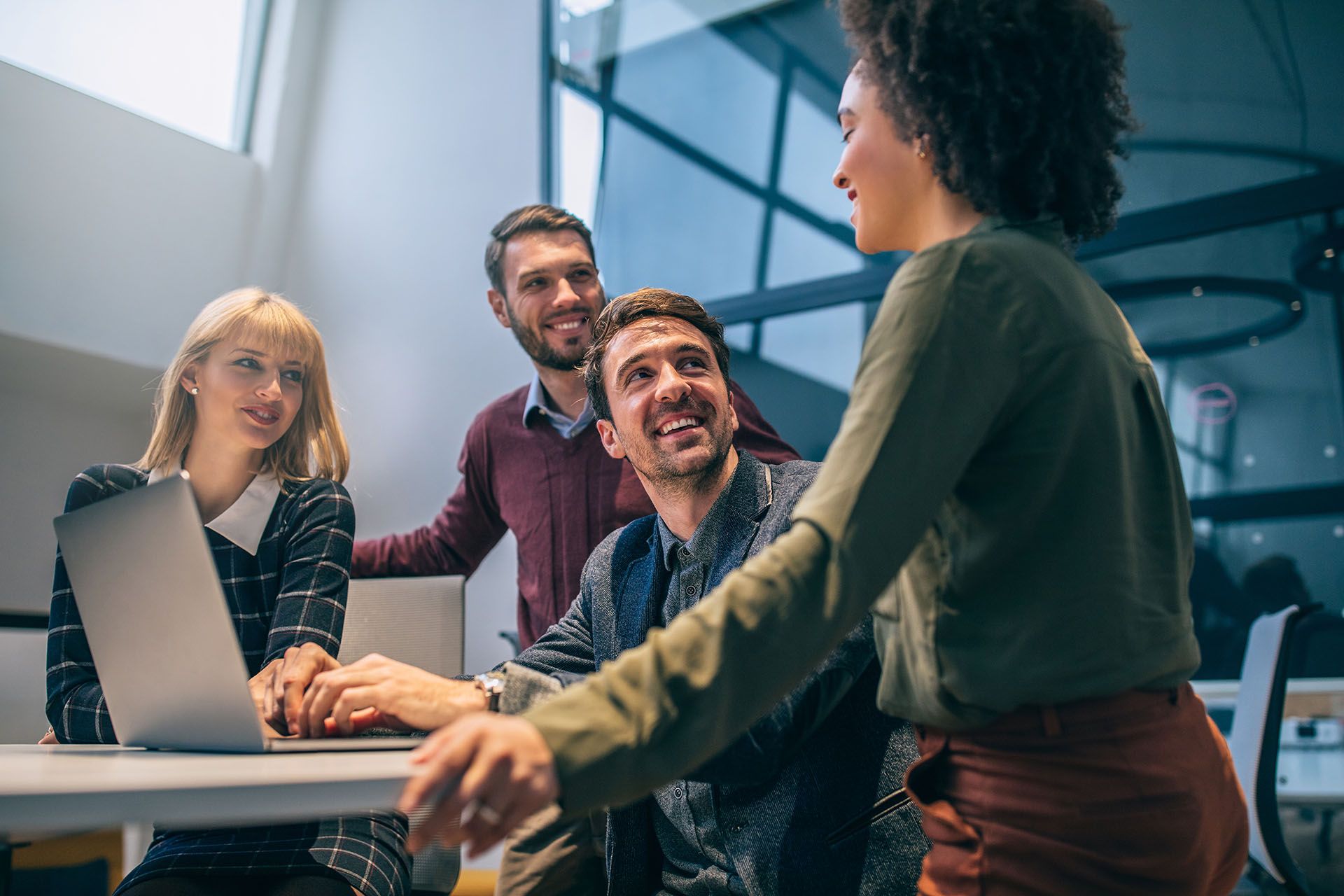 Group of coworkers collaborating around a laptop, smiling in an office setting.
