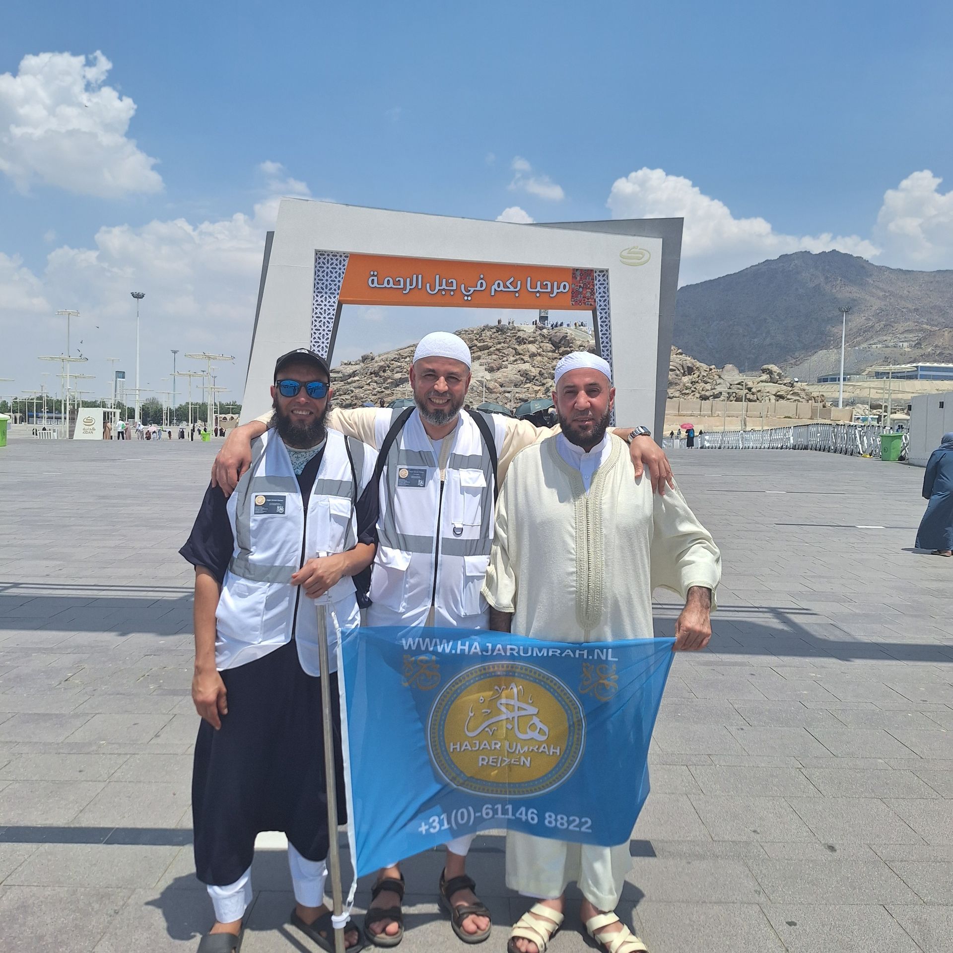 Drie mannen poseren voor een foto terwijl ze een blauwe vlag vasthouden