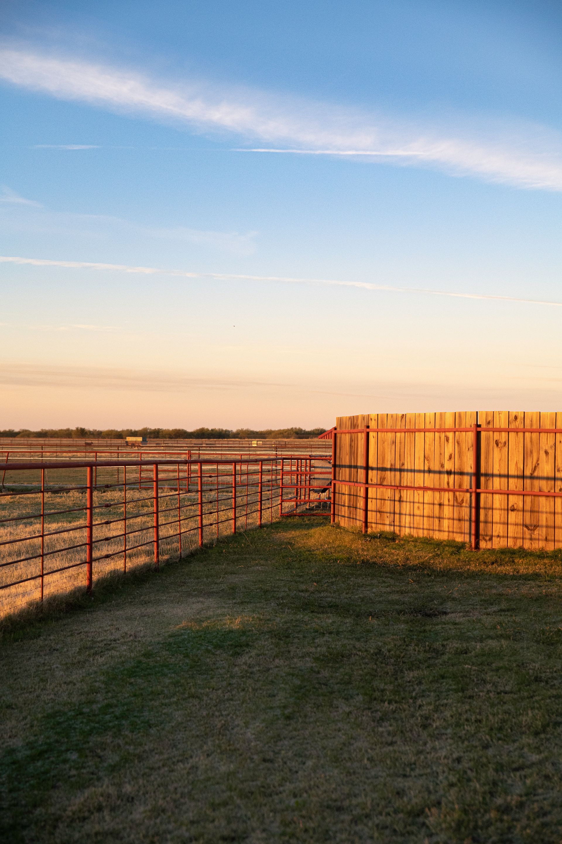 a wooden fence surrounds a grassy field with a sunset in the background .