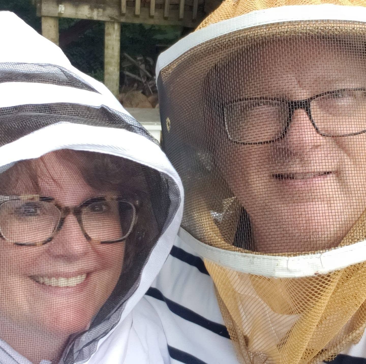 Two smiling people wearing beekeeping veils and glasses standing outdoors