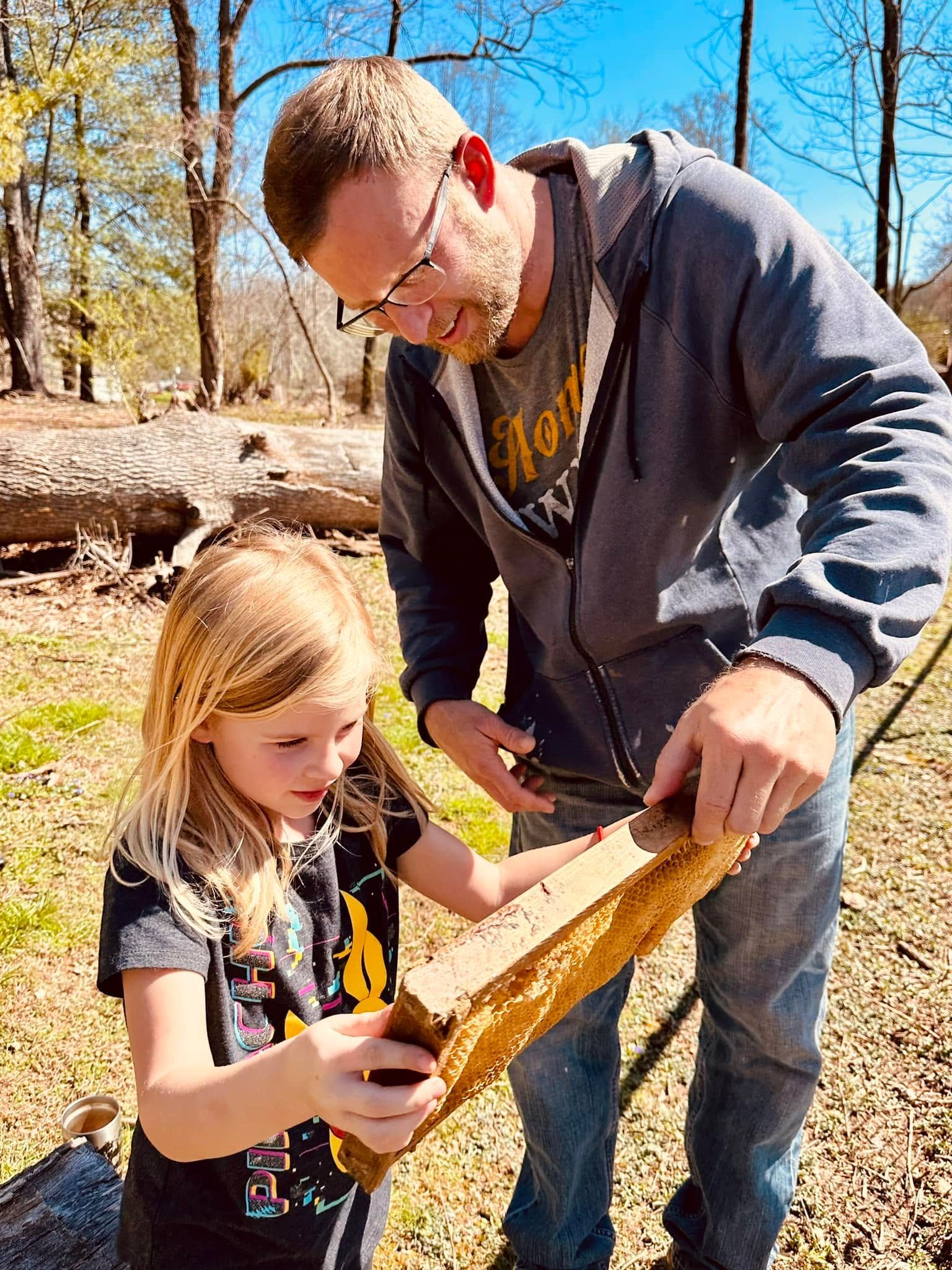 Adult and child inspecting a large leaf outdoors in a wooded area