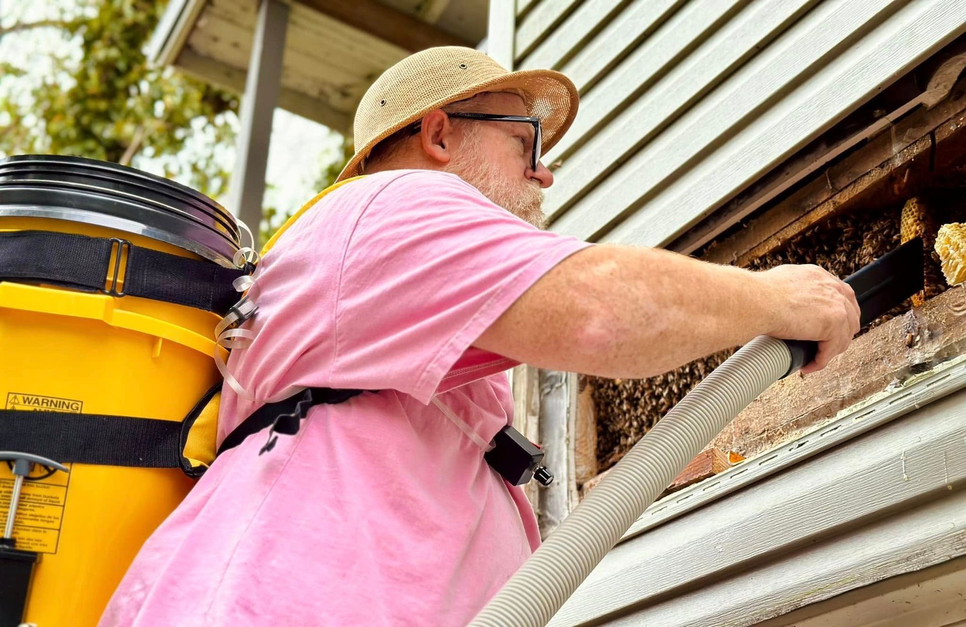 Worker in pink shirt using a hose to clean dirt from a house’s siding and window.
