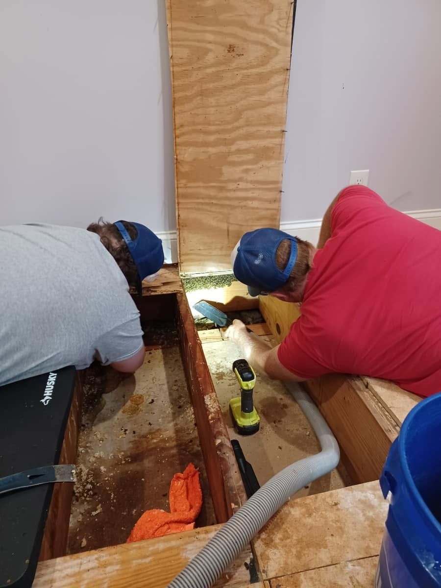 Two workers in blue caps crawl into a floor opening during home renovation.