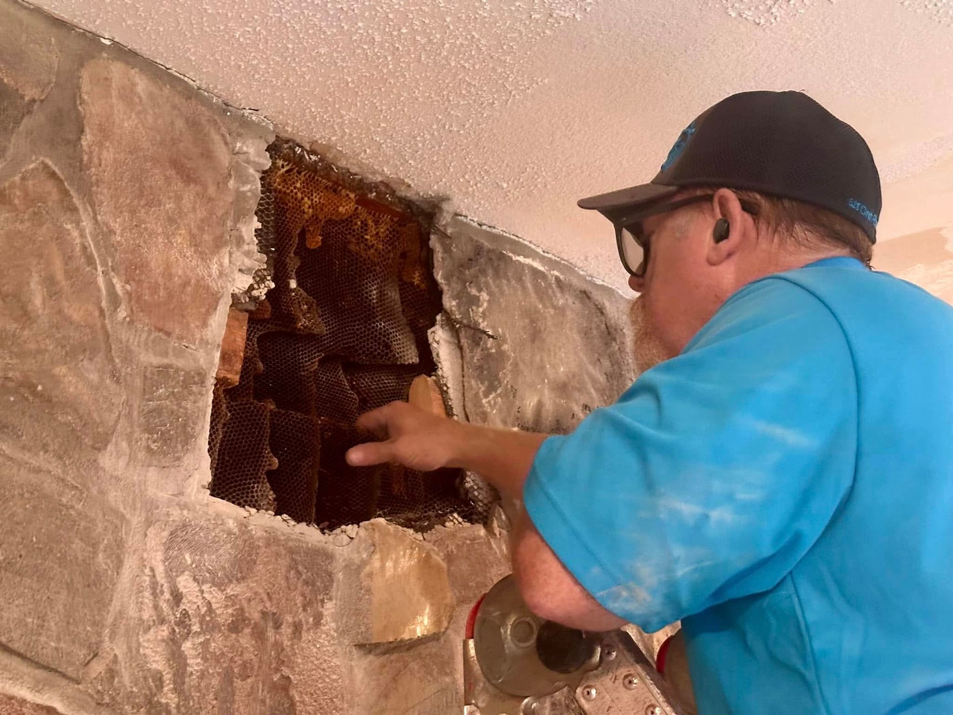 Worker in a blue shirt and cap inspecting damaged drywall inside a wall opening