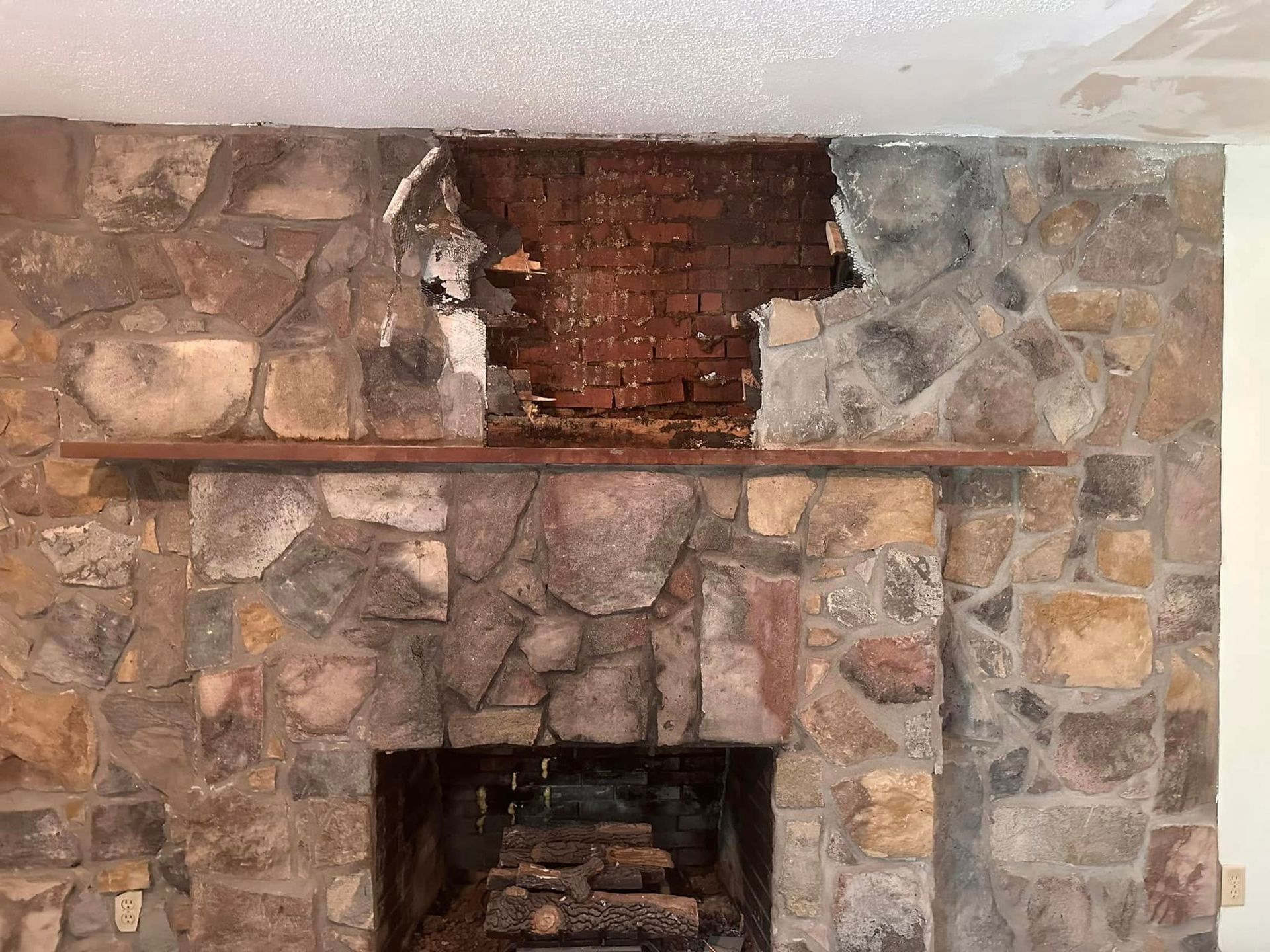 Stone fireplace with damaged brick opening and rough, uneven masonry surrounding it
