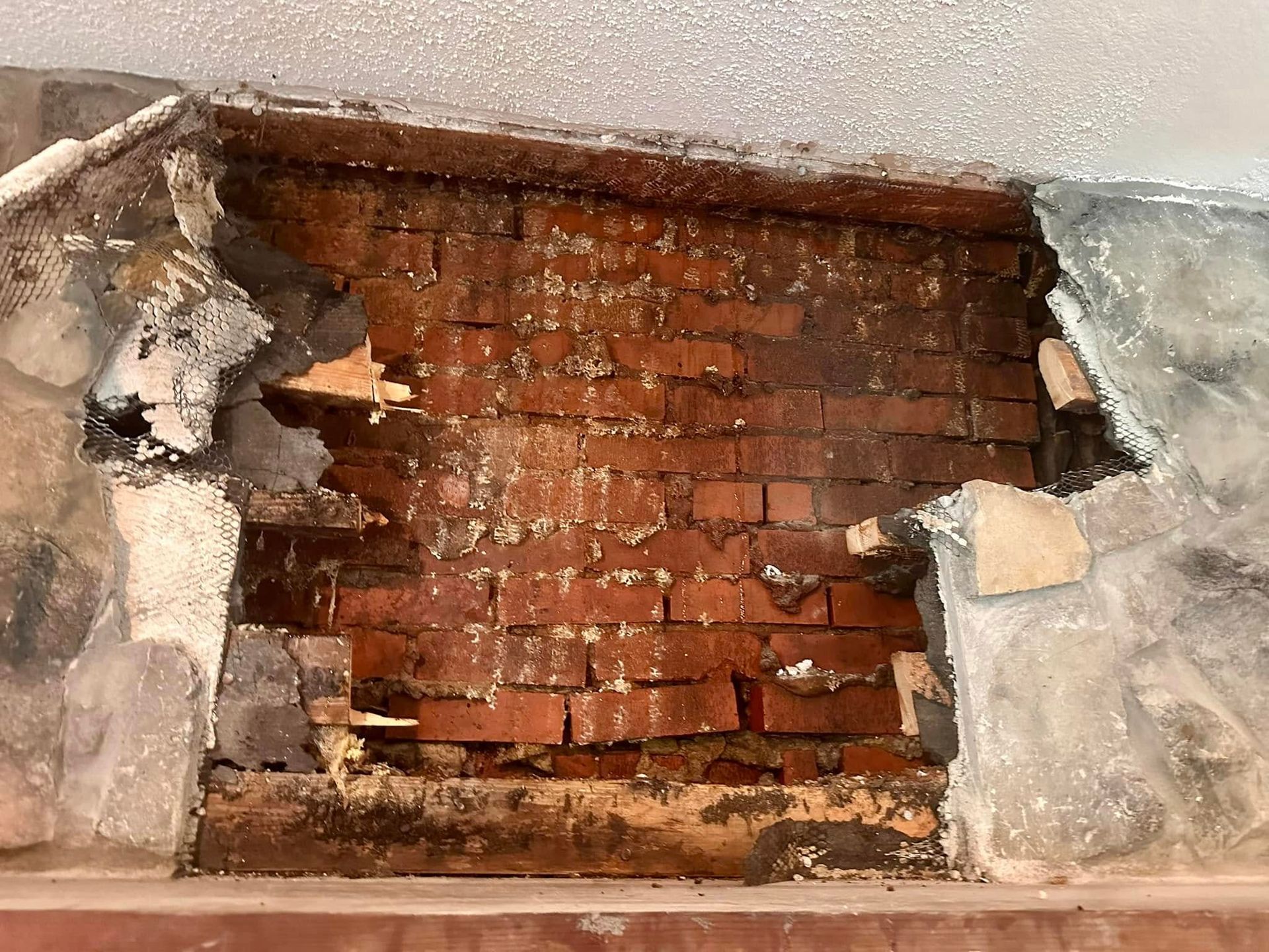Exposed red brick wall with damaged plaster and a rough rectangular opening