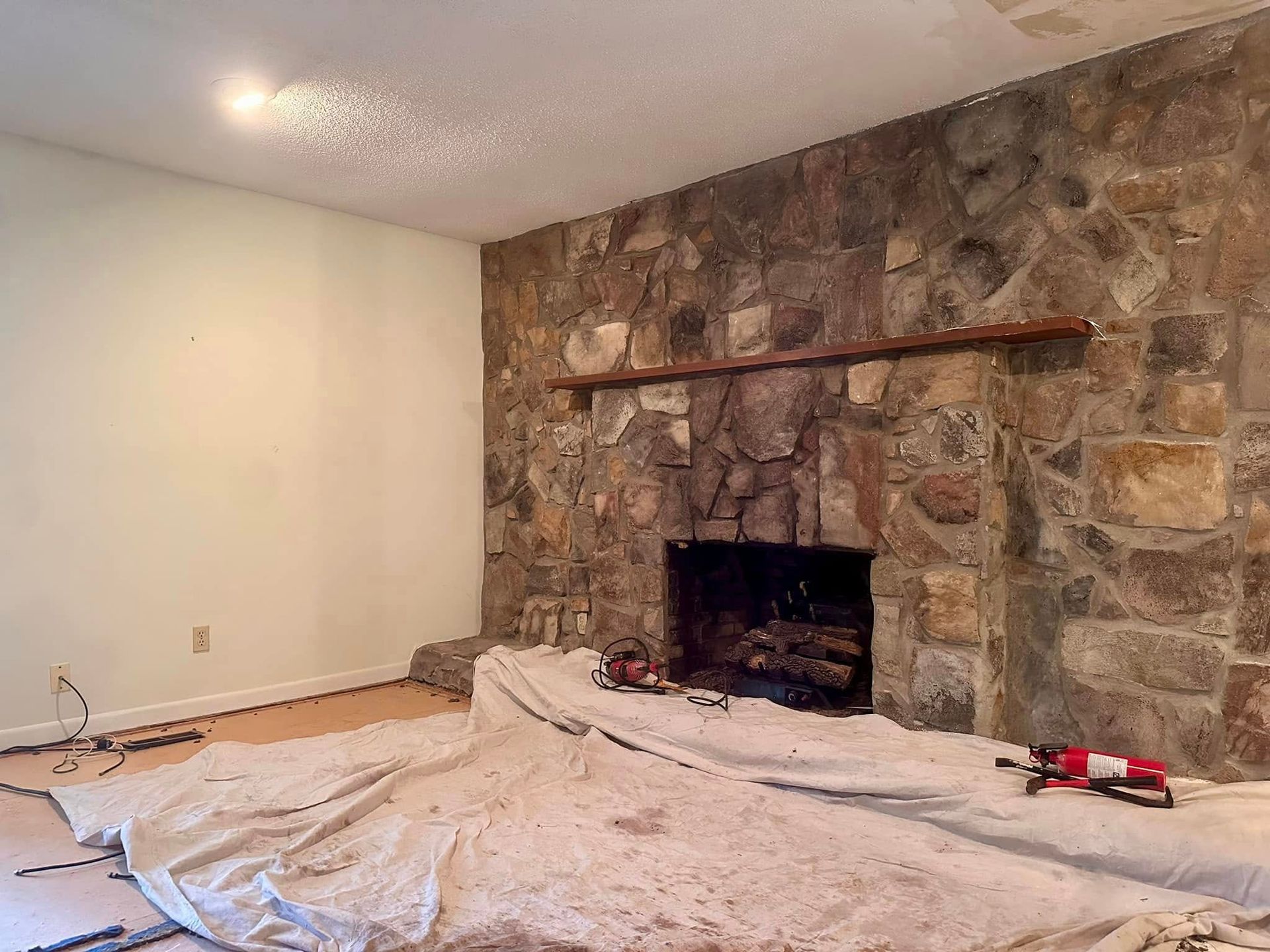Living room with stone fireplace, bare walls, and drop cloths covering the floor during renovation