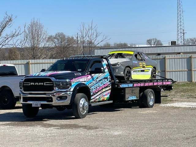 A tow truck is carrying a race car on the back of it.